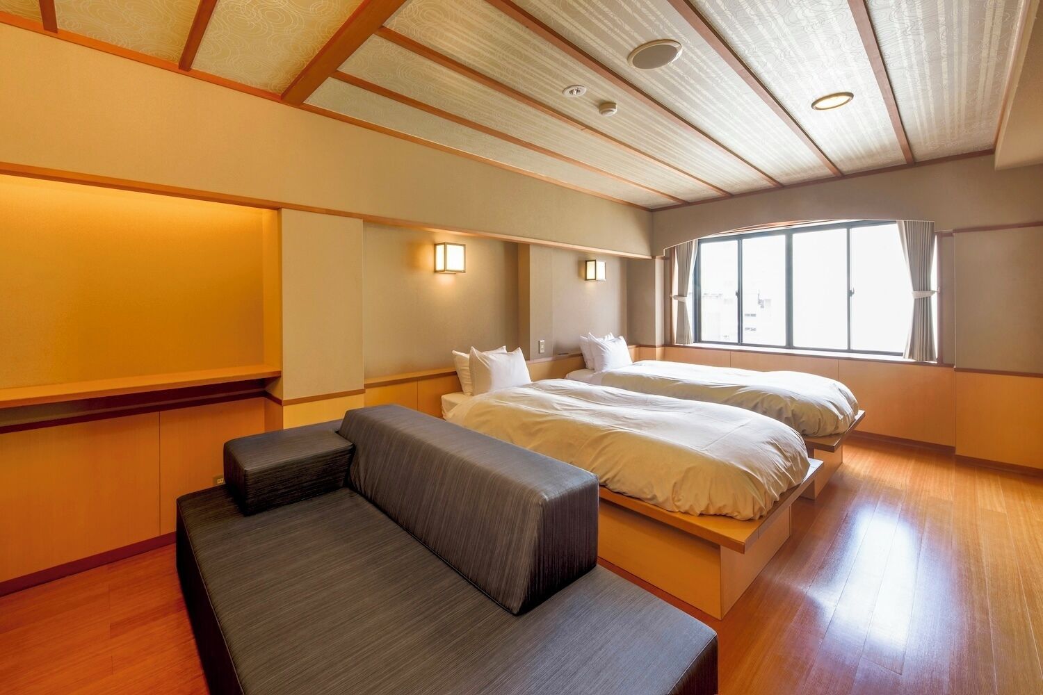 A hotel room with a bed, a sofa, a window with curtains, and a ceiling with wooden beams.