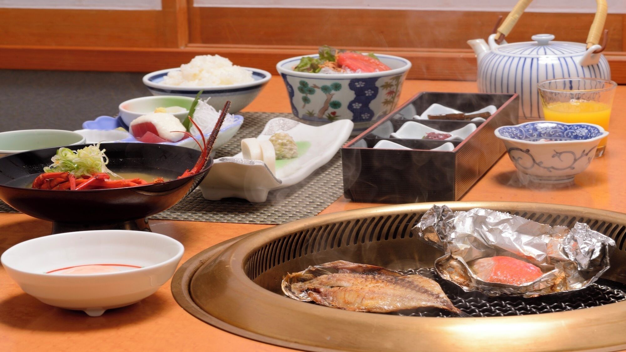 Een traditionele Japanse maaltijdopstelling met verschillende gerechten, waaronder een hete pot, rijst en een theepot.
