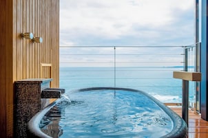 Un jacuzzi con vistas al océano, paneles de madera y barandilla de cristal.
