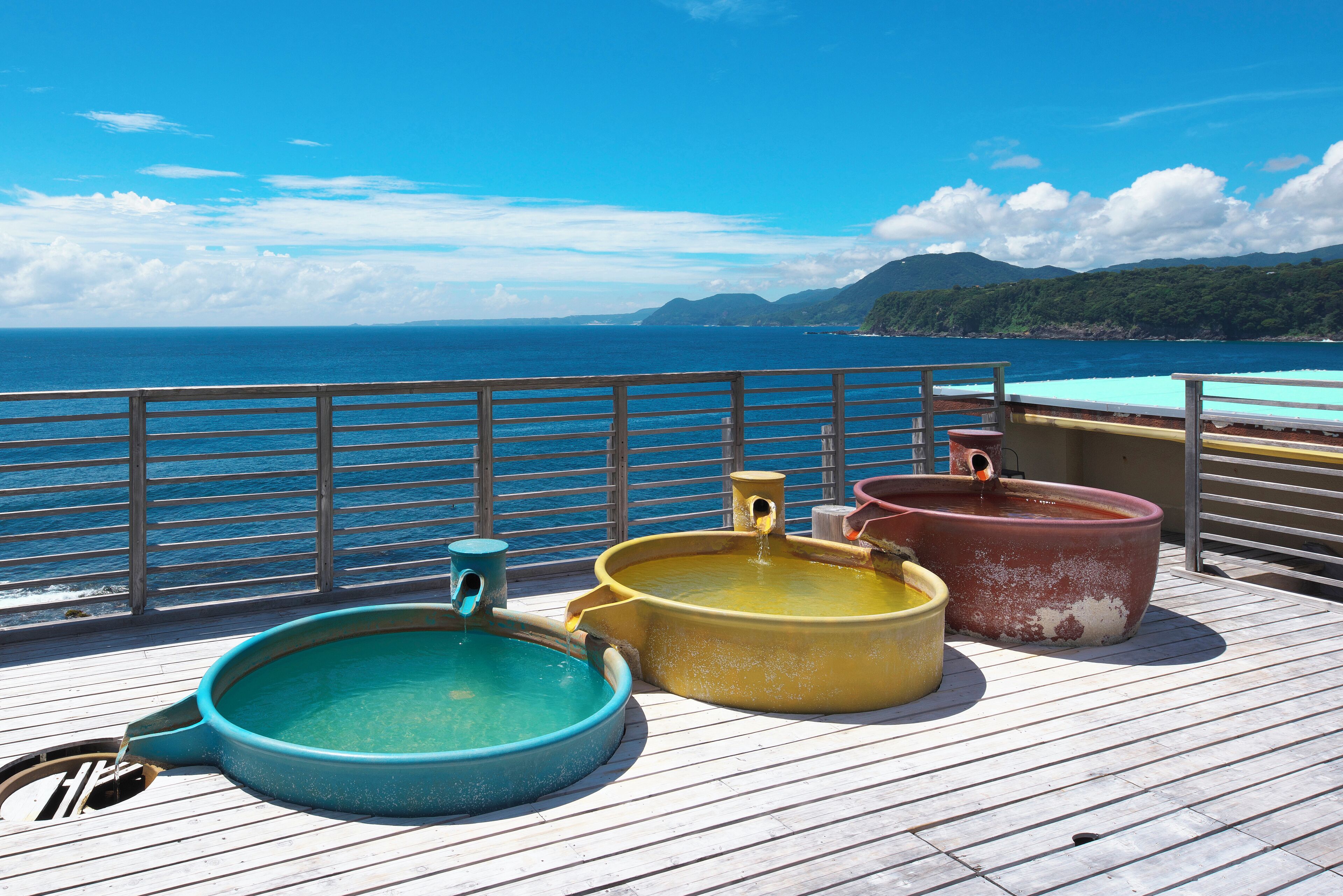 A deck with three hot tubs and a railing overlooking a body of water and mountains.