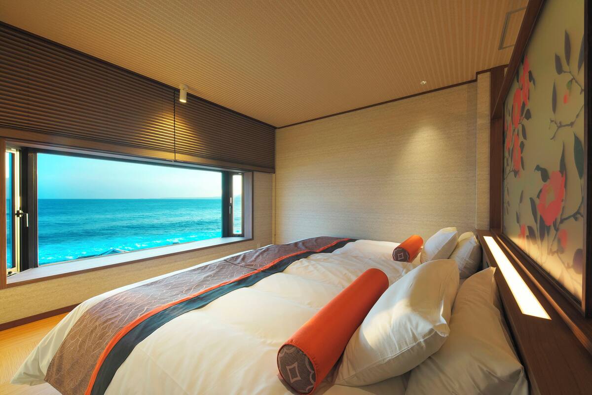 A bedroom with a large bed, a view of the ocean, and a painting on the wall.
