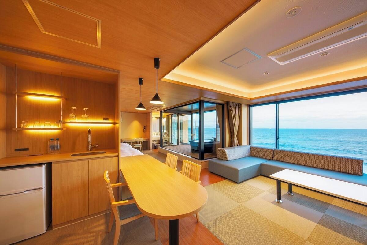 A modern interior with a wooden kitchen, dining area, and a seating area with a view of the sea.
