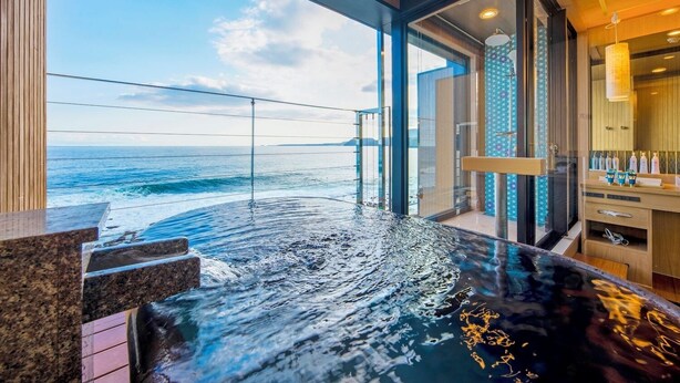 A modern infinity pool with a view of the ocean, a glass-enclosed bathroom, and a wooden deck. - Senoumi (Higashiizu)