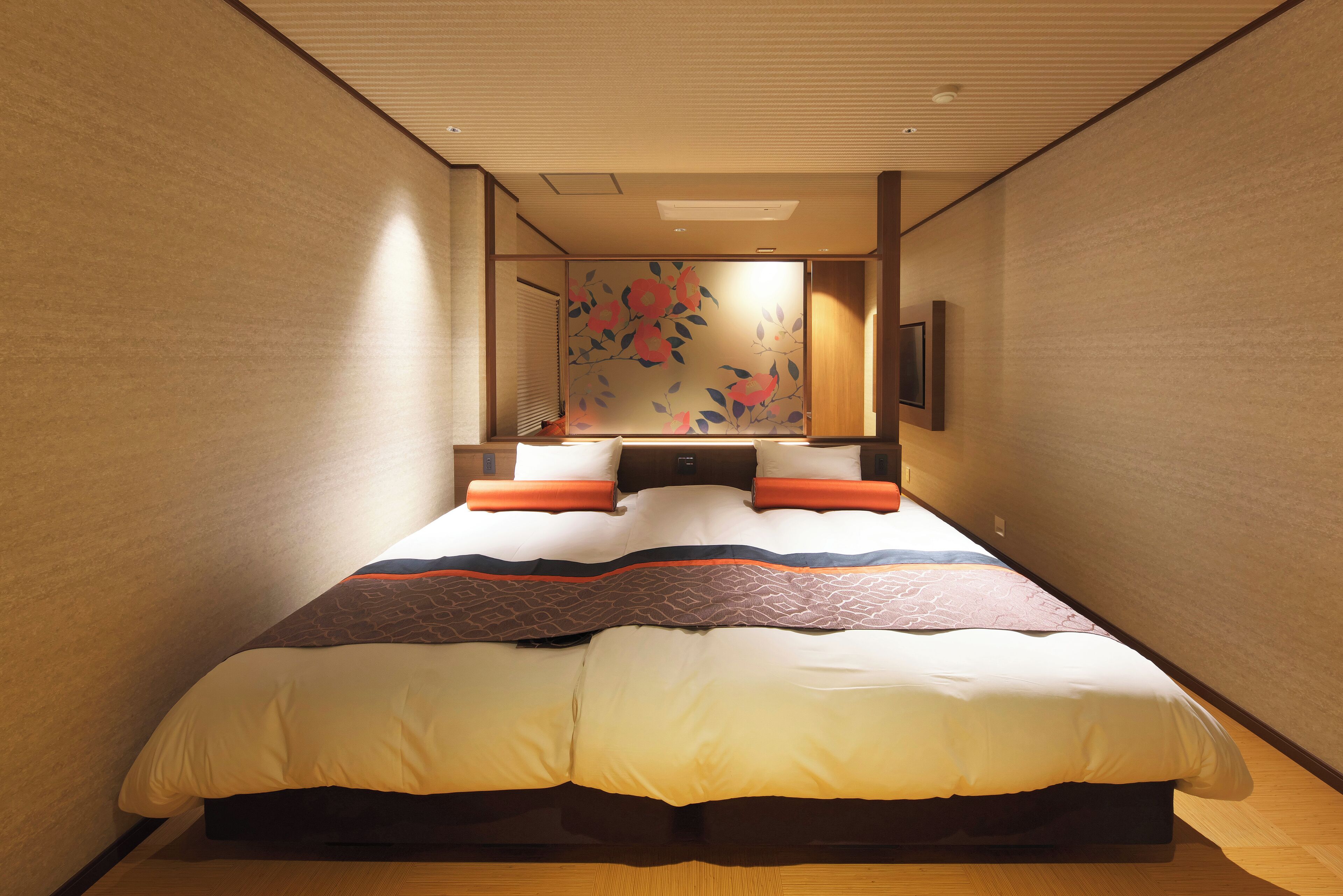 Une chambre avec un grand lit, un plancher en bois, un téléviseur fixé au mur et une porte coulissante ornée d’un motif floral.