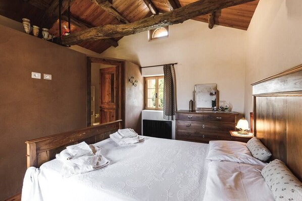 Un dormitorio con techo de madera, una cama grande con ropa blanca, un aparador y un espejo.