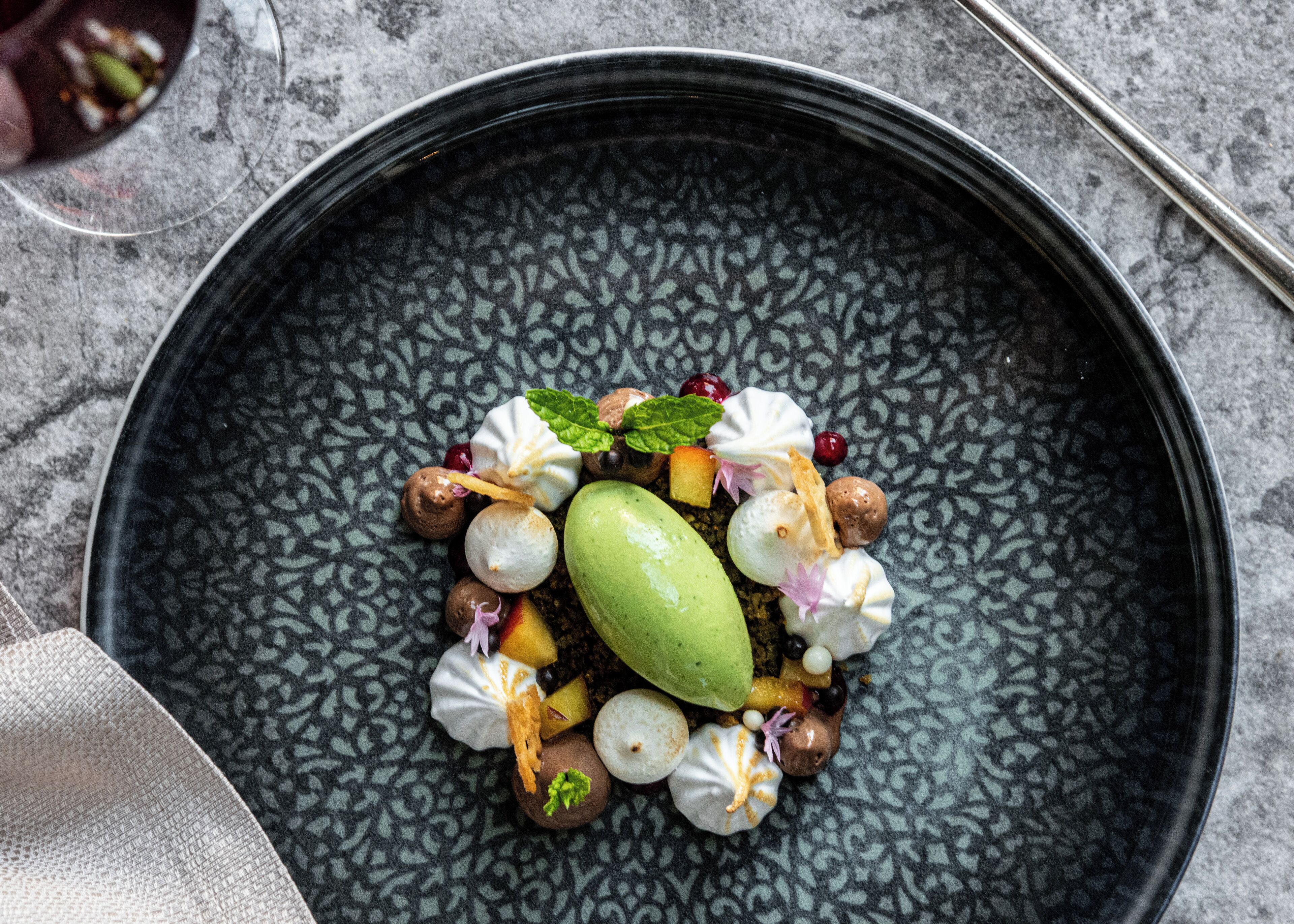Un plato de postres con diversos dulces y frutas sobre una bandeja oscura y texturizada.