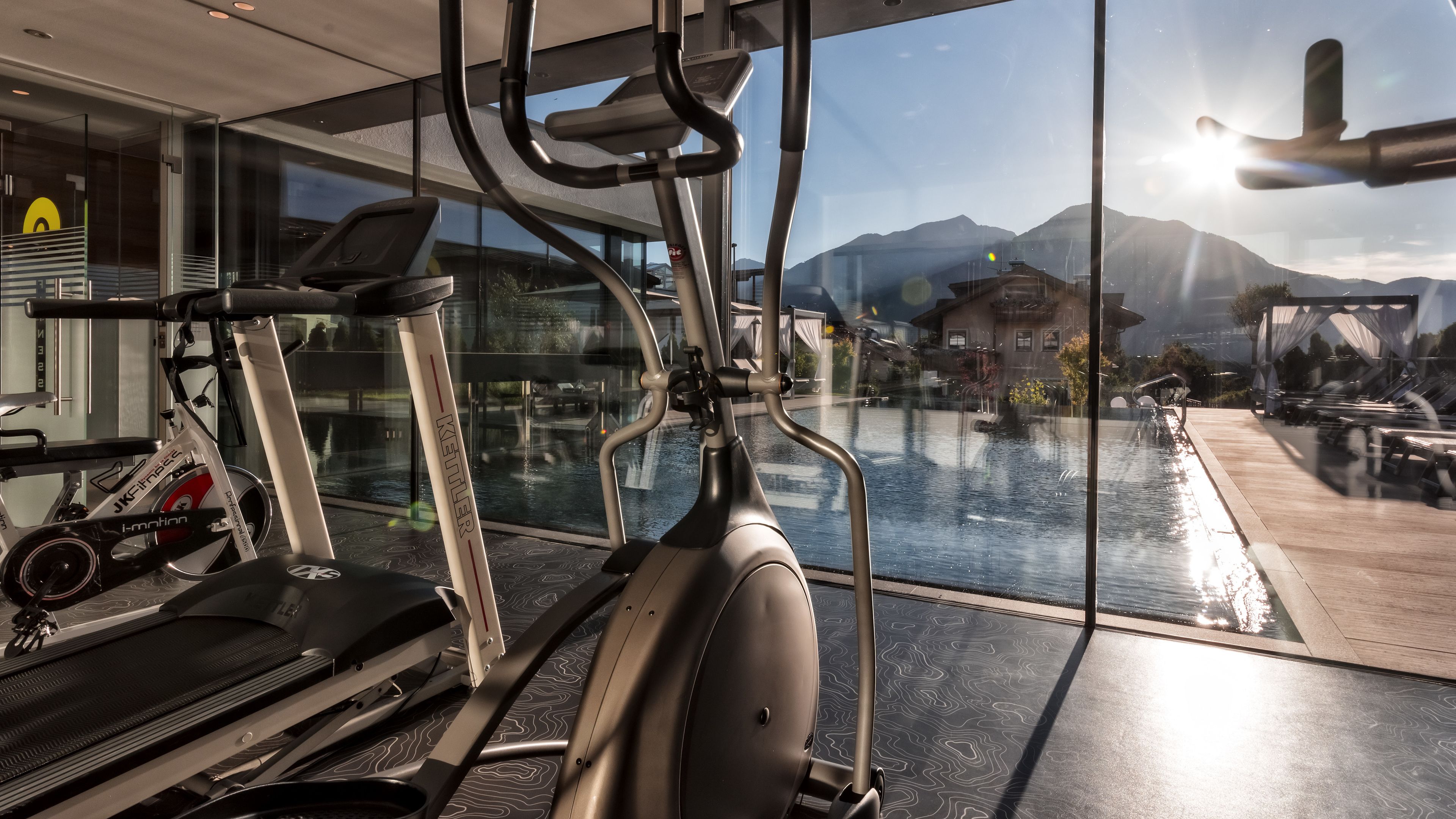 Une salle de sport équipée de matériel d’exercice, notamment des tapis de course et des vélos d’appartement, et offrant une vue sur une piscine et des montagnes grâce à de grandes fenêtres.