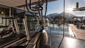 Une salle de sport équipée de matériel d’exercice, notamment des tapis de course et des vélos d’appartement, et offrant une vue sur une piscine et des montagnes grâce à de grandes fenêtres.