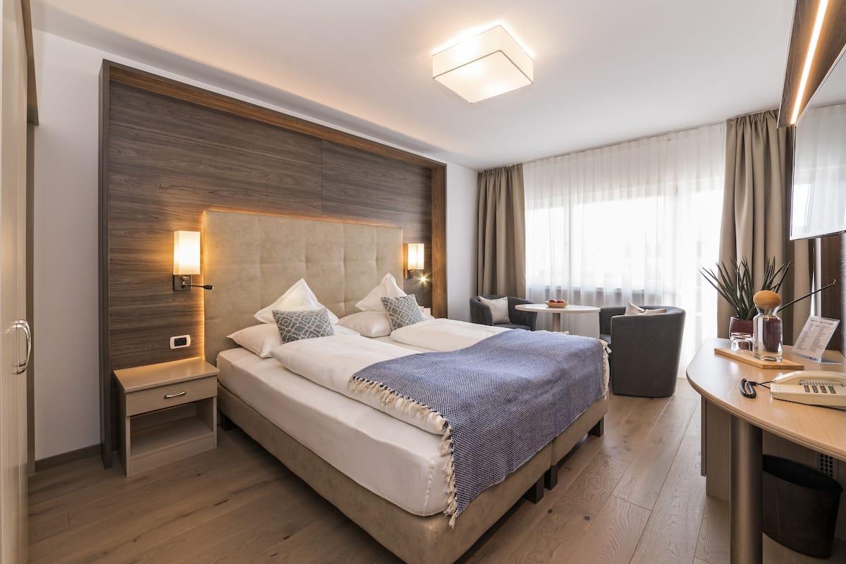 A modern hotel room with a large bed, bedside tables, a desk with a chair, and a view of the city.