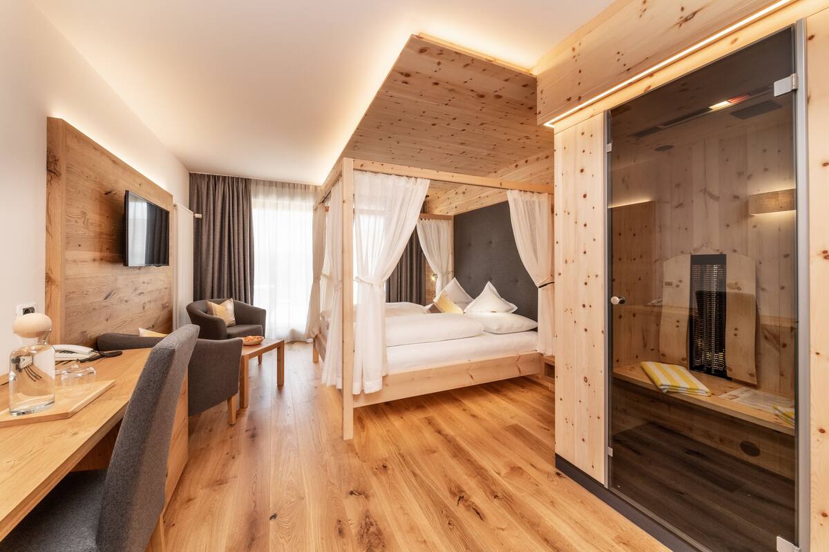 A modern room with a wooden ceiling, a bed with white bedding, a desk with a chair, and a TV mounted on the wall.