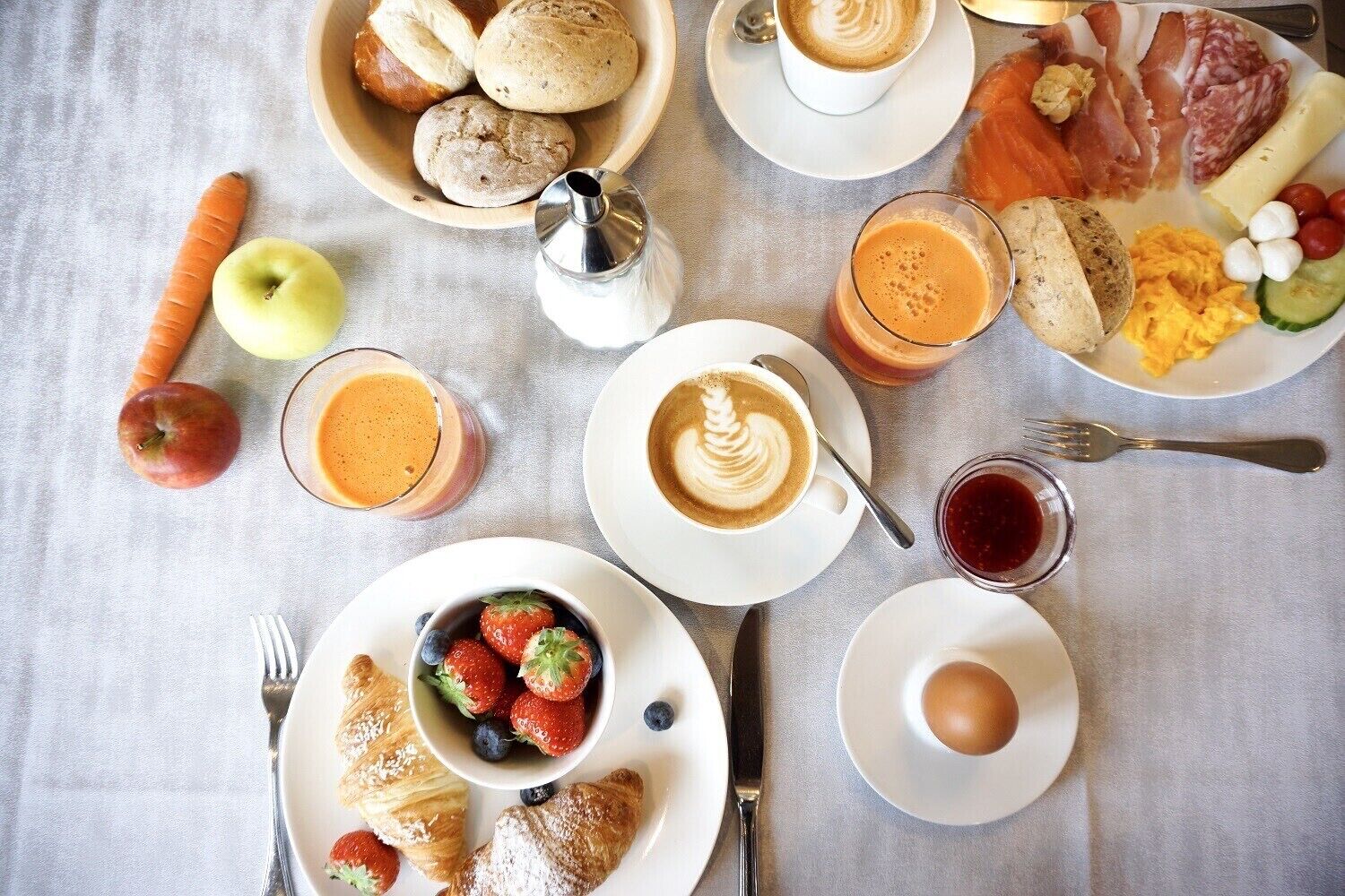 Un desayuno con cruasanes, huevos, café y diversas frutas y verduras sobre una mesa.