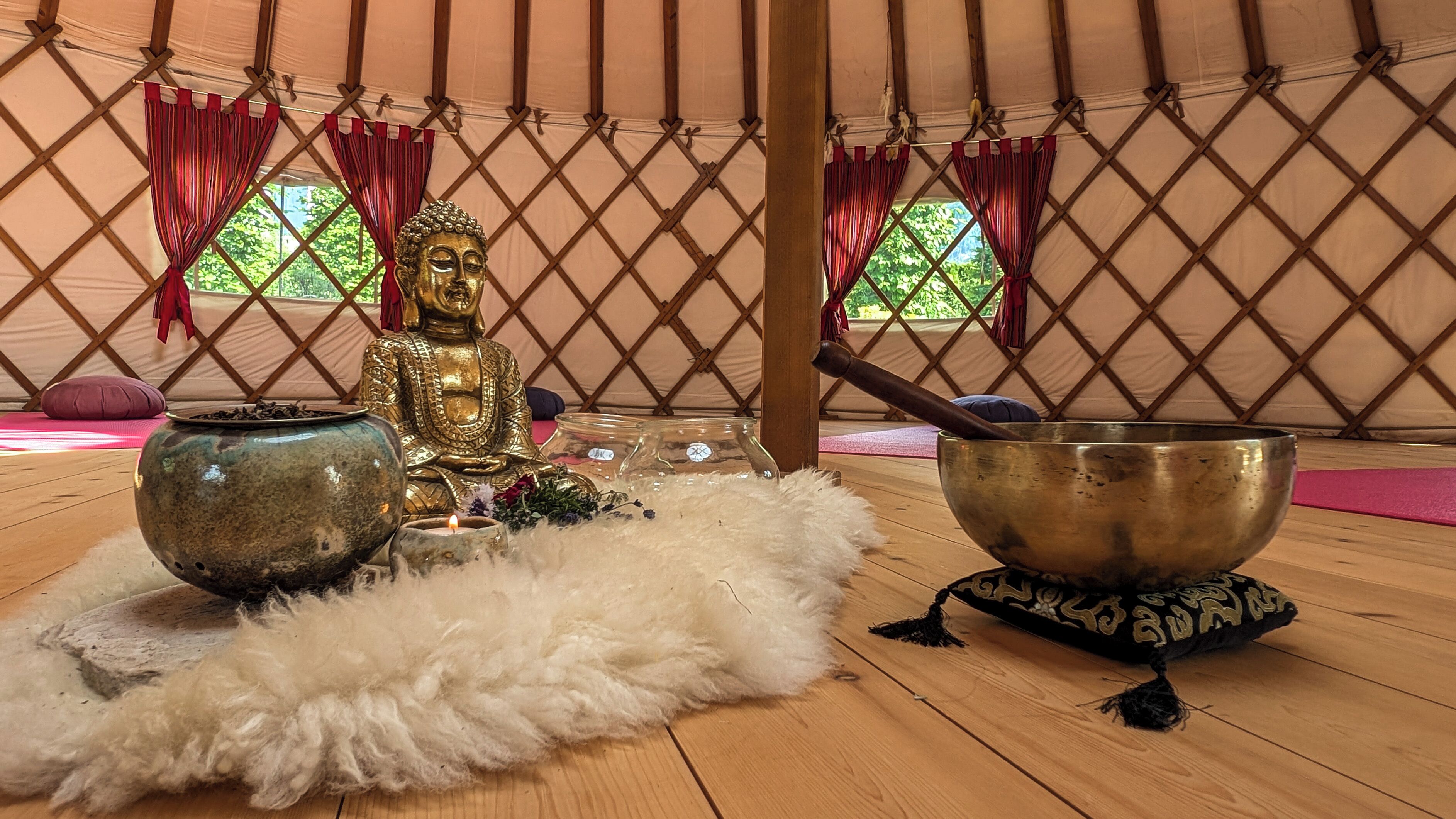 Ein Meditationsraum mit einer goldenen Statue, einem großen Gong und einer Schale auf einer Matte.