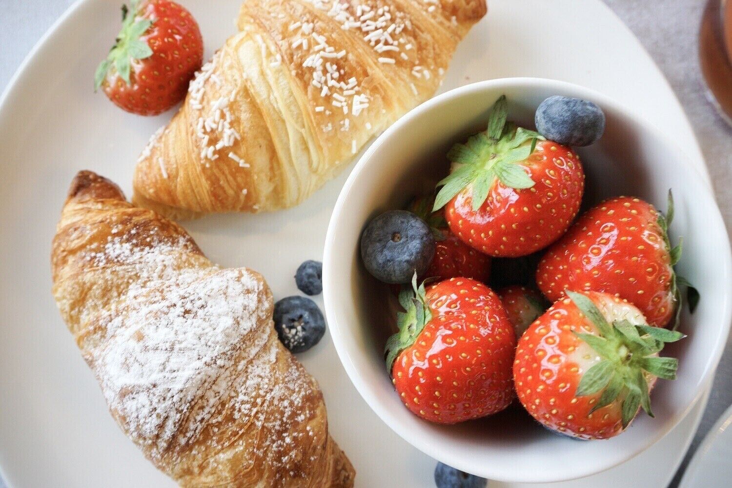 En tallrik med croissanter och en skål med jordgubbar och blåbär.