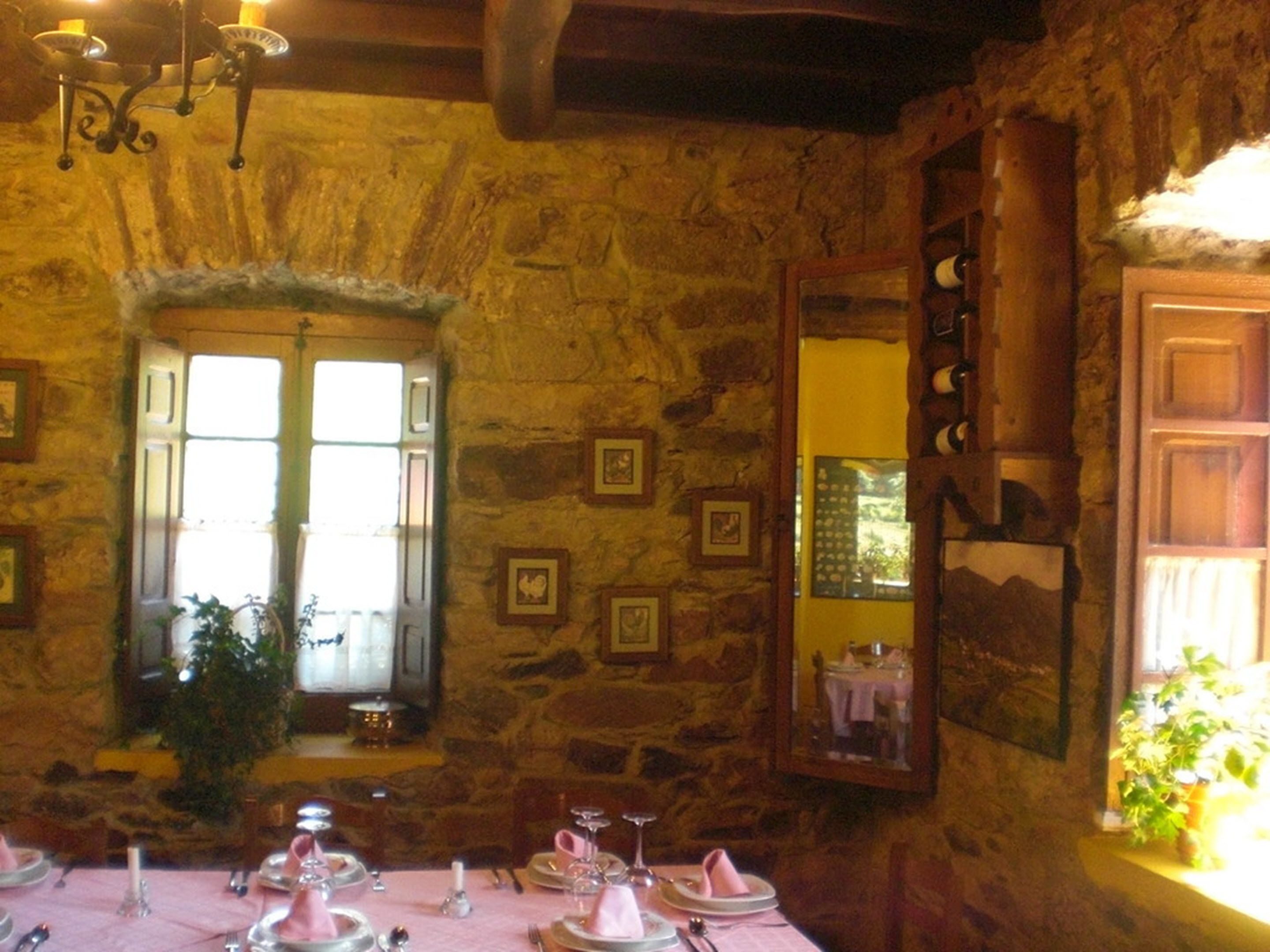 A dining area with stone walls, framed pictures, and a window with curtains.
