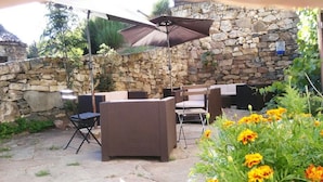 An outdoor patio with wicker furniture, a stone wall, and a large umbrella. - Hotel Rural Genestoso (Cangas del Narcea)