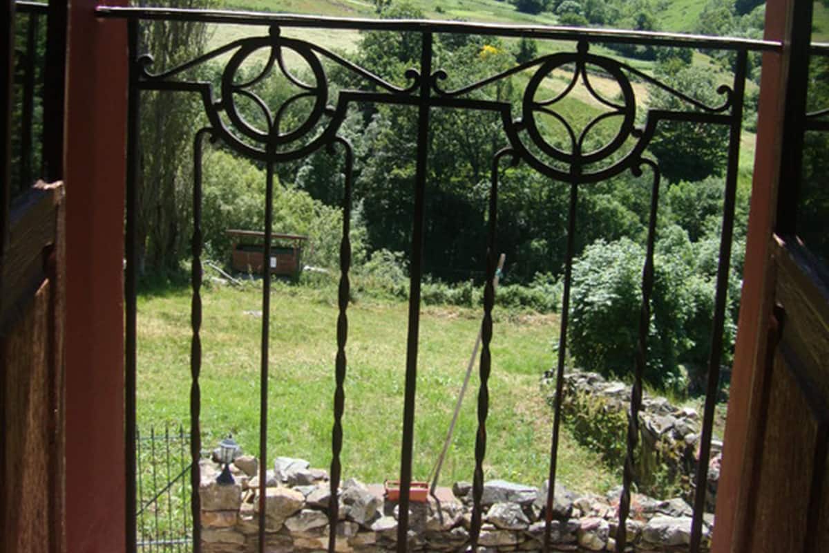 A balcony with wrought iron railings overlooking a green valley and hills.