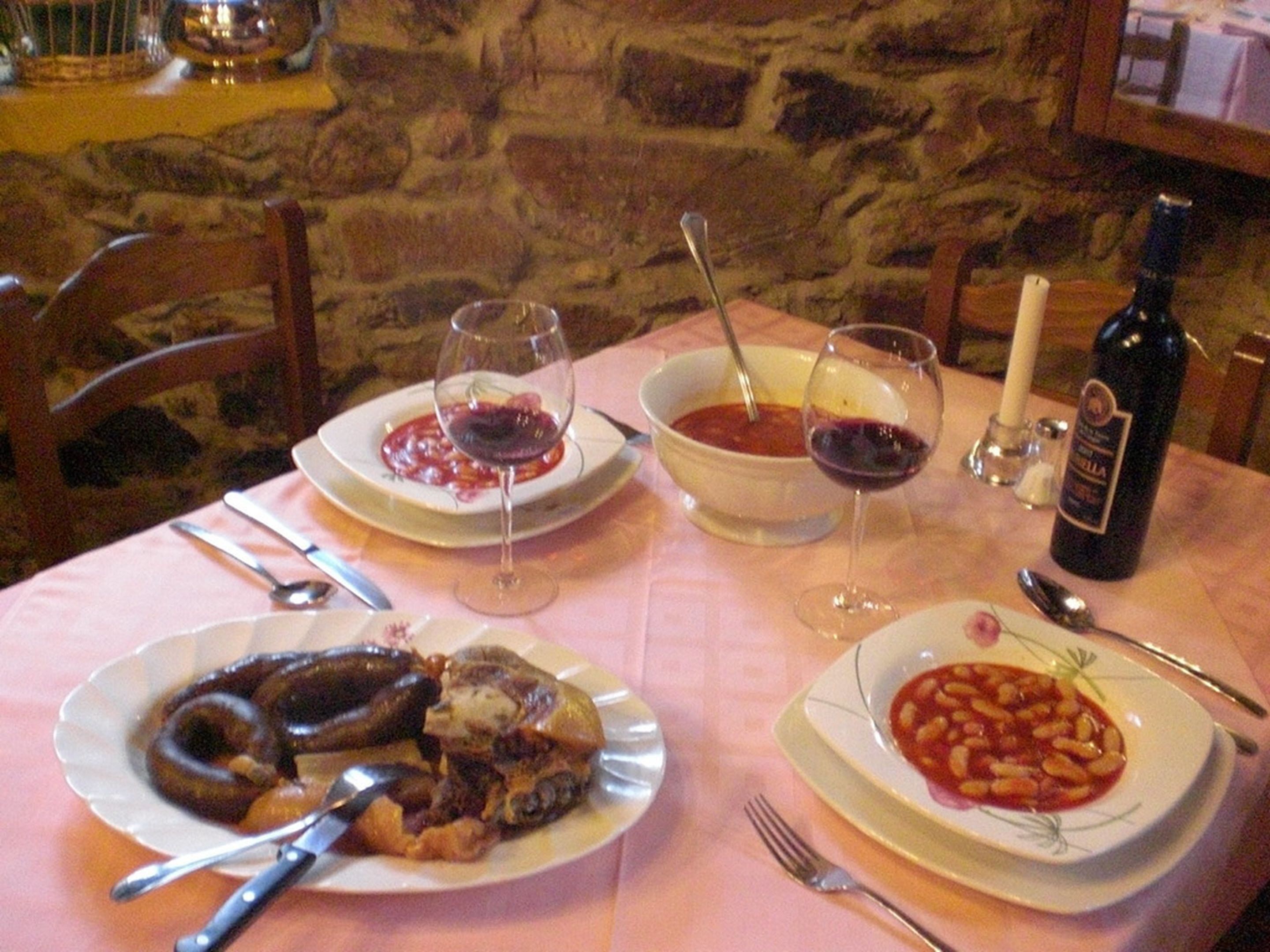 A table set with plates of food, glasses of red wine, and a bottle of wine.