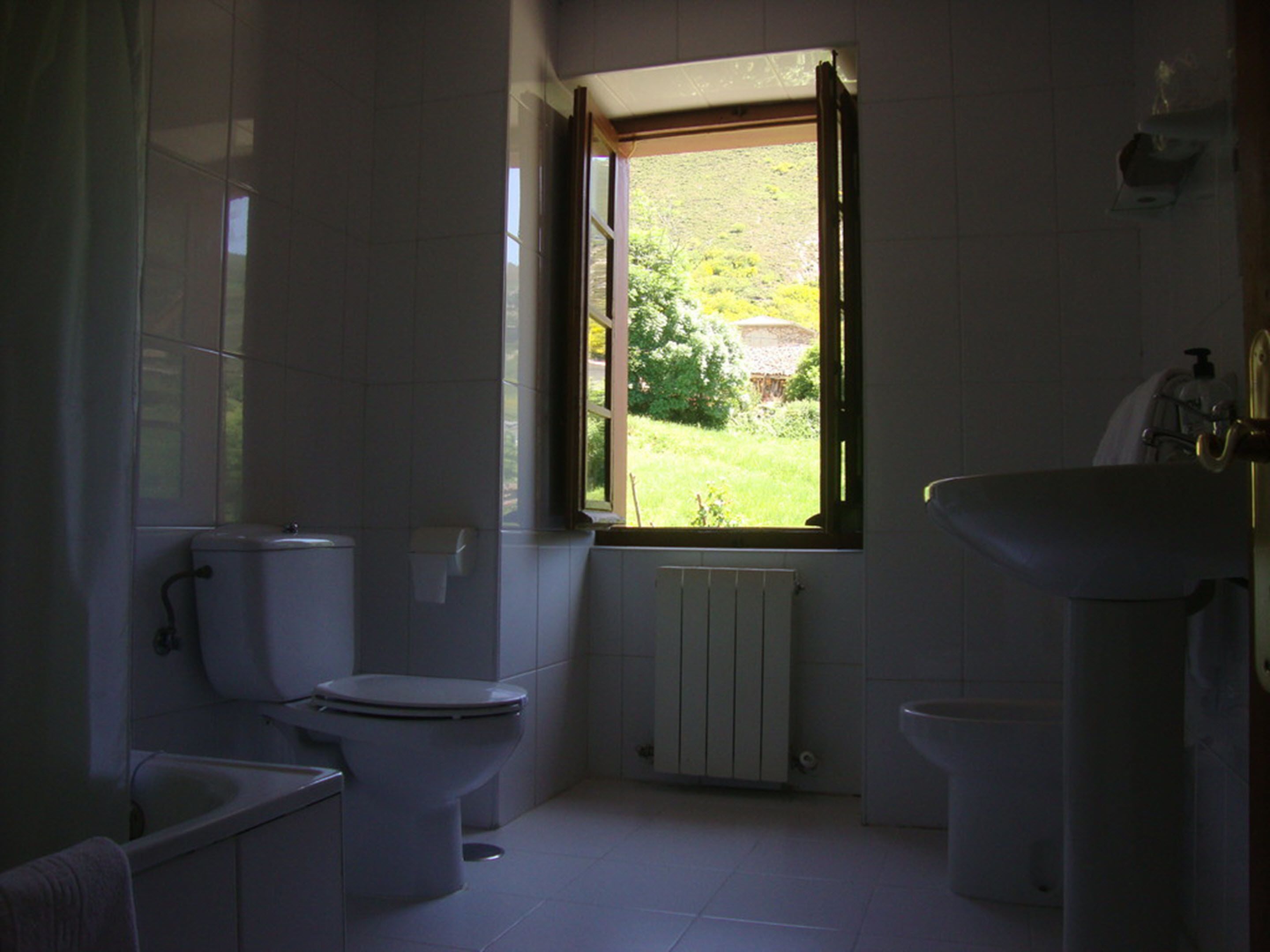 A bathroom with a toilet, a sink, and a window with a view of greenery outside.