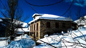 A stone building with a snow-covered roof, surrounded by snow and bare trees. - Hotel Rural Genestoso (Cangas del Narcea)