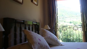 A bedroom with a bed, two pillows, a nightstand, a lamp, and a window with a view of a mountainous landscape. - Hotel Rural Genestoso (Cangas del Narcea)