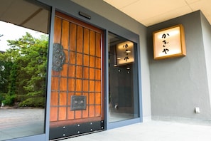 A traditional wooden door with a grid pattern, a modern glass entrance, and a sign with Japanese characters.