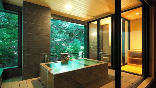 A modern bathroom with a large bathtub, a glass shower enclosure, and a view of lush greenery outside. - Kagiya the annex of Senoumi (Minamiizu)