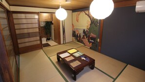 Una habitación tradicional japonesa con suelo de esteras de tatami, una mesa de madera baja con papeles, una lámpara colgante y un mural en la pared.