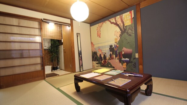 Una habitación con tatamis, una mesa de madera baja, una lámpara colgante y una pintura tradicional japonesa en la pared.