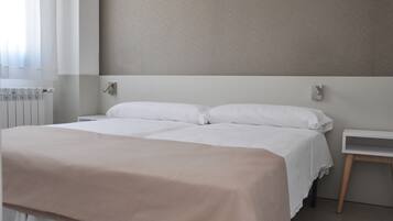 A hotel room with a large bed, a bedside table, a radiator, and a wall-mounted light fixture.