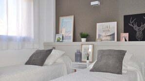 Habitación de hotel con dos camas, una mesita de noche con lámpara, aire acondicionado instalado en la pared, y varias imágenes y adornos enmarcados.