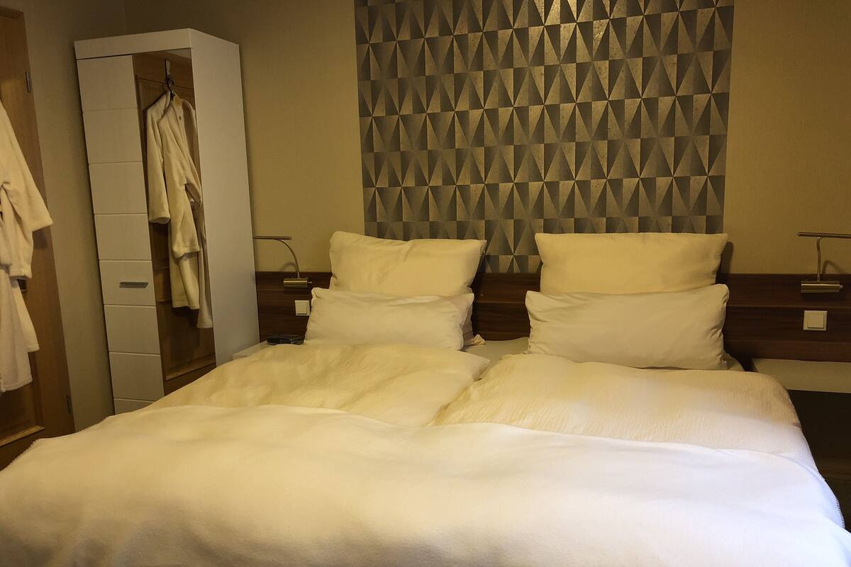 A hotel room with a bed, a wardrobe, and a patterned wall.