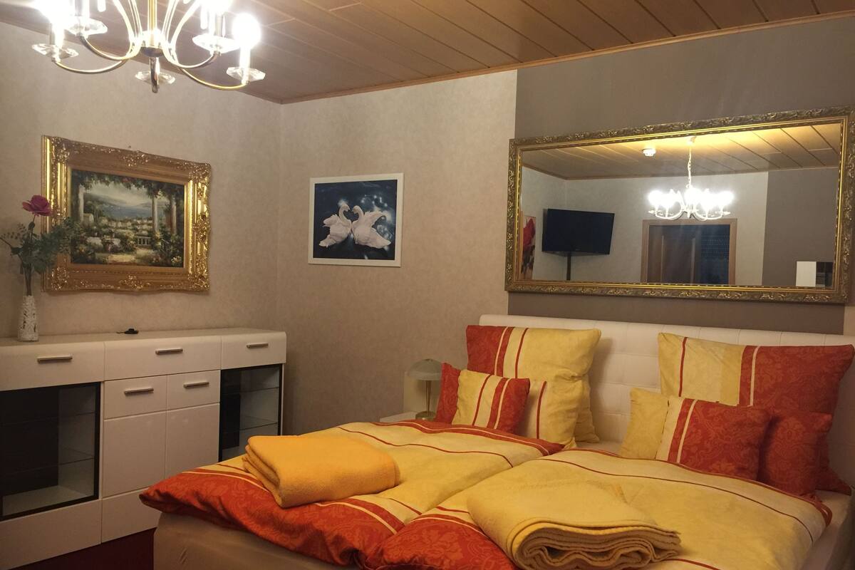 A hotel room with a bed, a dresser, a mirror, and a chandelier.