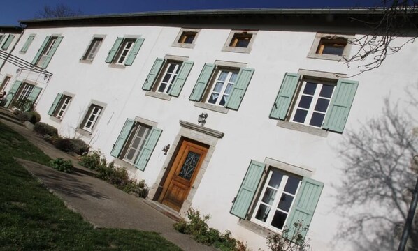 Un edificio blanco con contraventanas verdes, una puerta de madera central y varias ventanas.