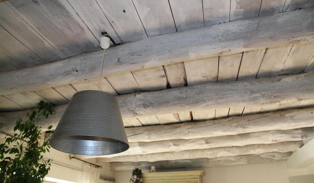 Een rustiek plafond met zichtbare houten balken en een hangende metalen lamp.