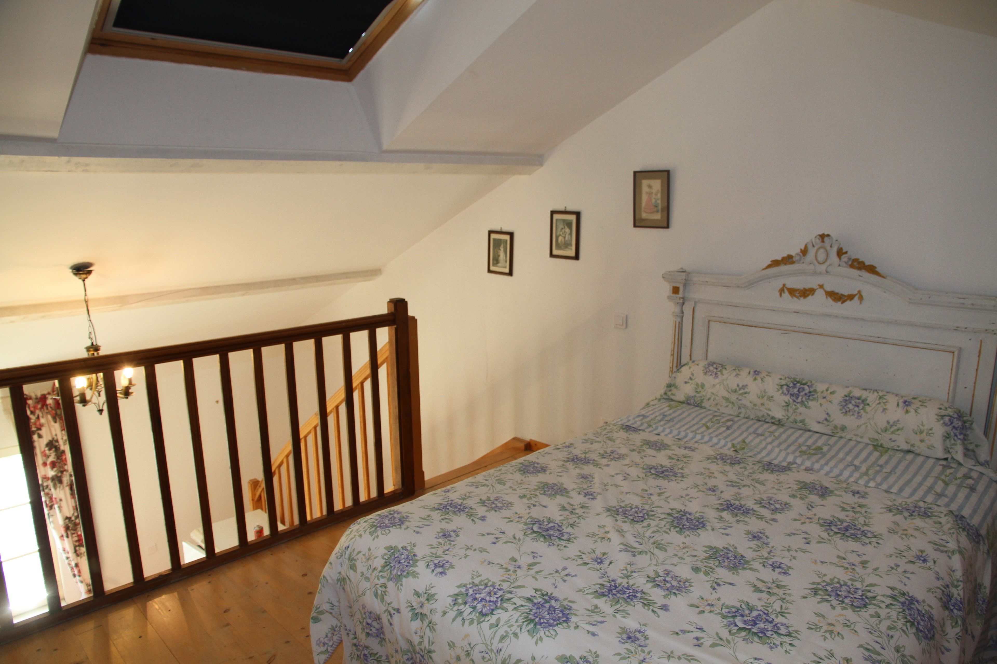 A bedroom with a bed, a wooden staircase, and a skylight.