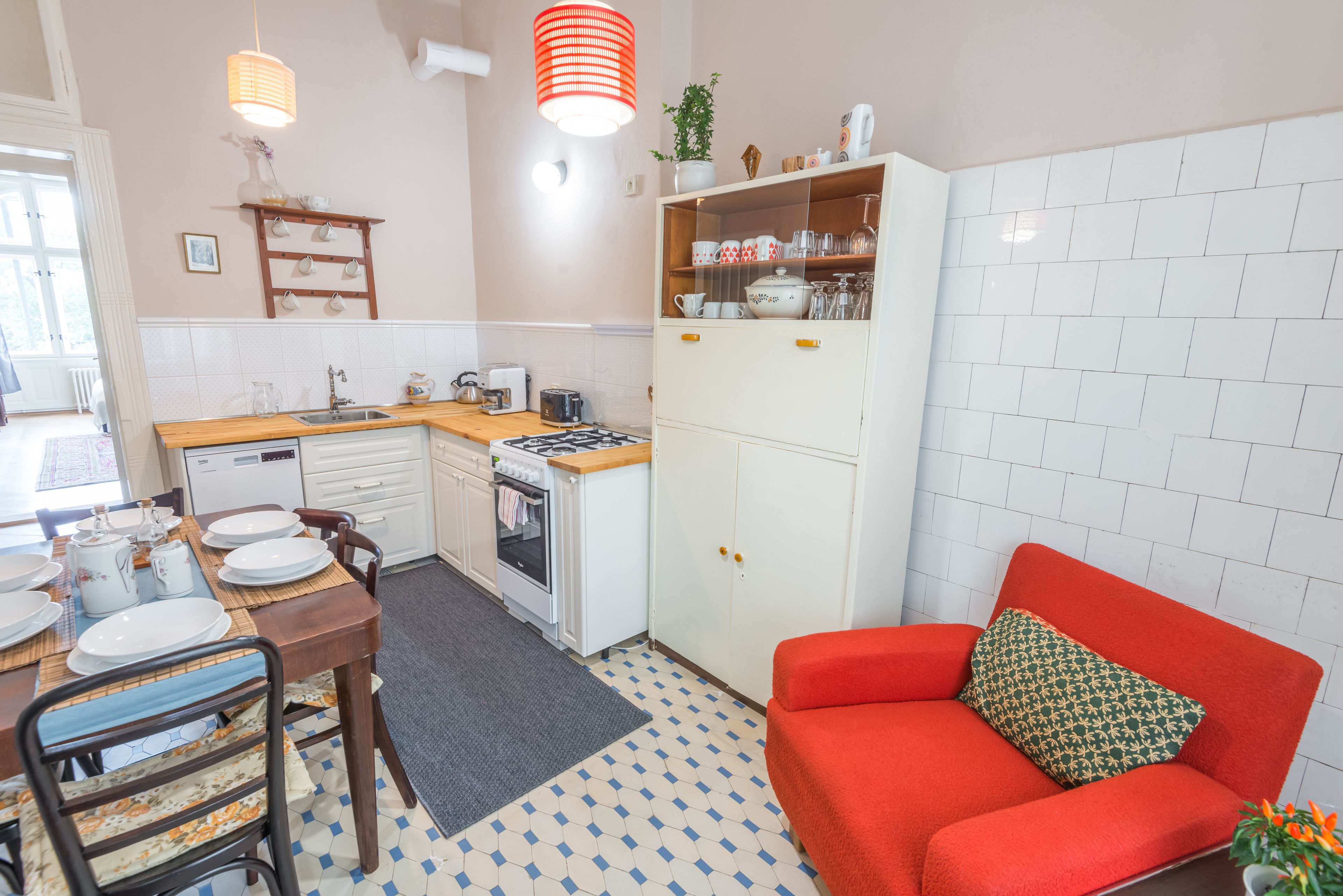 A compact kitchen with a dining table, chairs, a red sofa, and a tiled floor.