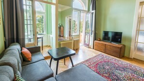A living room with a sofa, a small table, a television on a wooden cabinet, and a patterned rug. - Riverside Apartment With A Balcony (Prague)