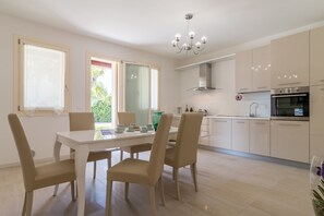 A modern kitchen with white cabinets, a dining table with four chairs, and a chandelier. - Cimadolmo Prosecco and History (Cimadolmo)