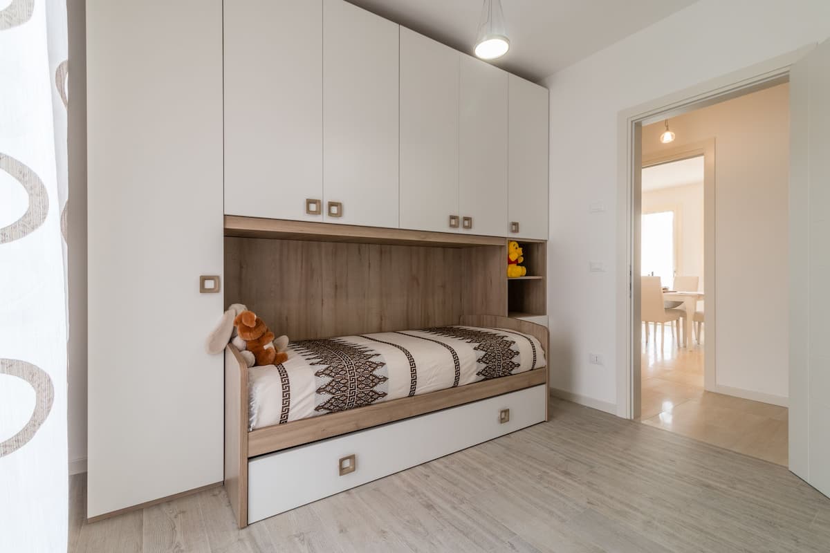 Quarto com cama, roupeiro embutido e chão de madeira.