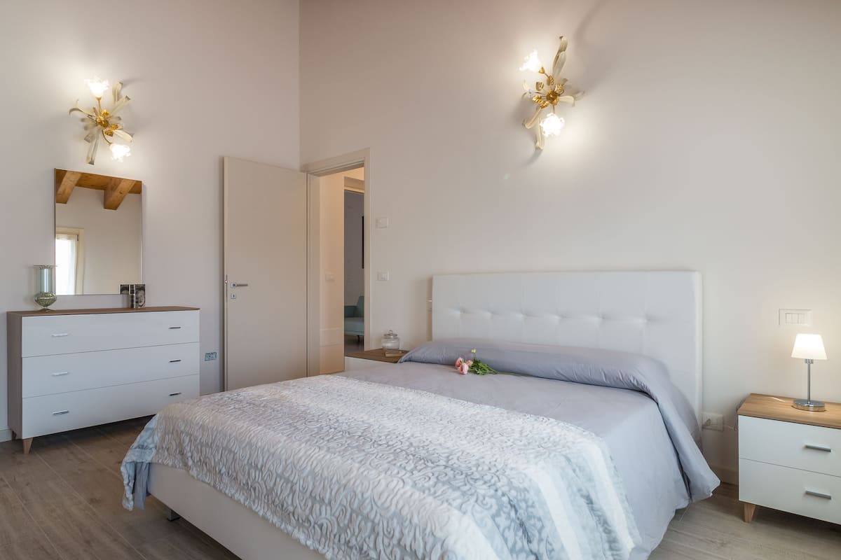 Quarto com cama, penteadeira, mesa de cabeceira e espelho.