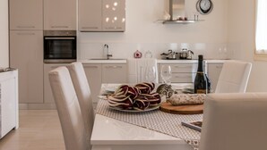A modern kitchen with white cabinets, a built-in oven, and a dining area with a table set for two. - Cimadolmo Prosecco and History (Cimadolmo)