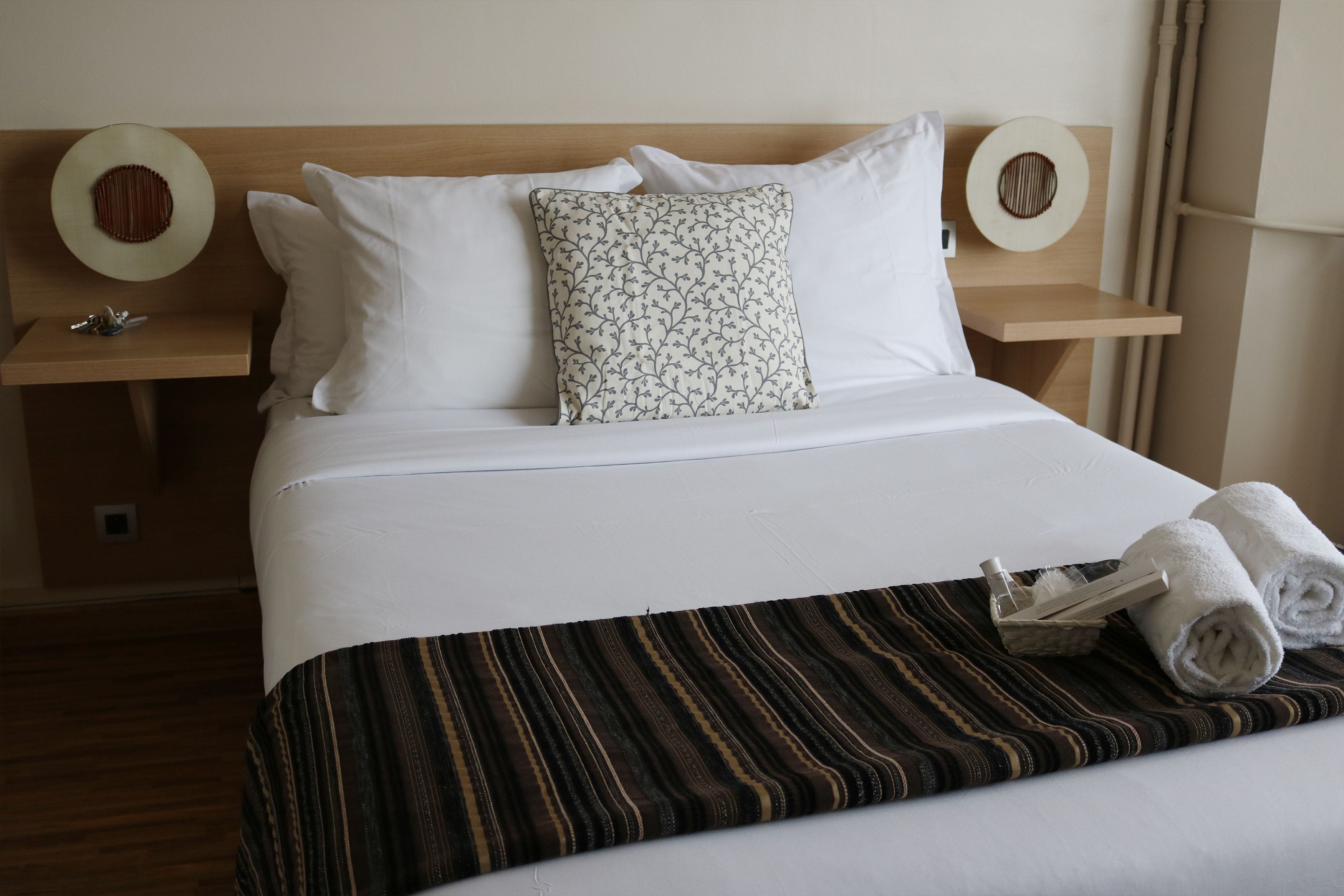 A neatly made bed with white linens, a striped throw blanket, and two rolled towels on the bed.