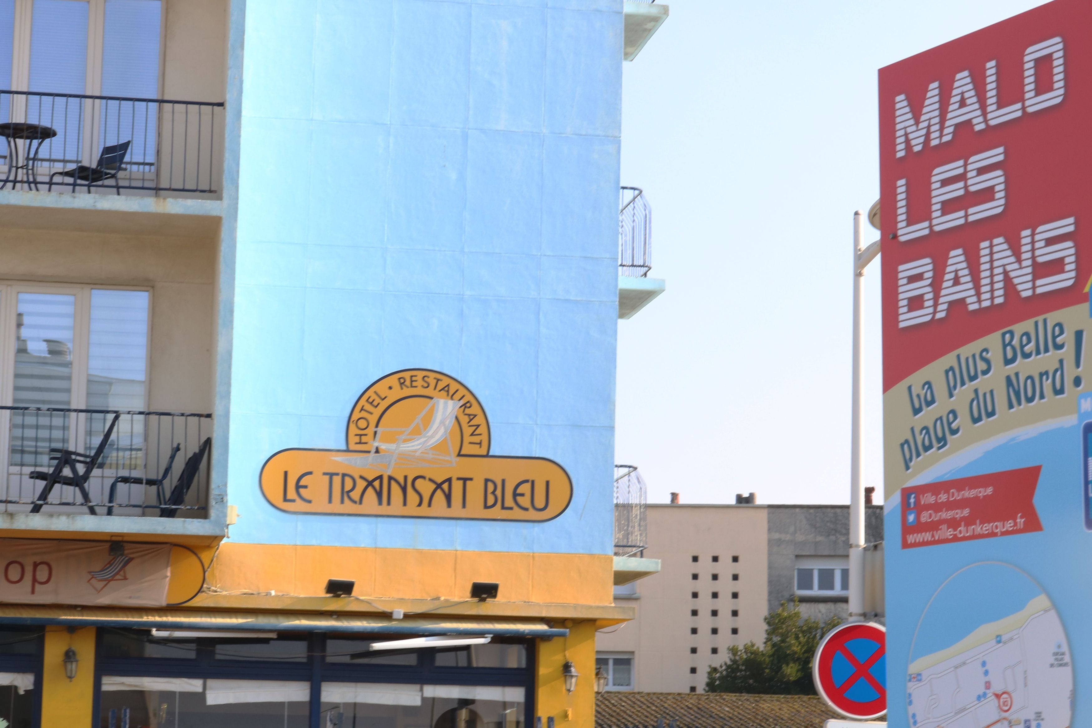 A hotel sign with a blue and yellow color scheme, featuring a logo and the name 'Le Transat Bleu'.