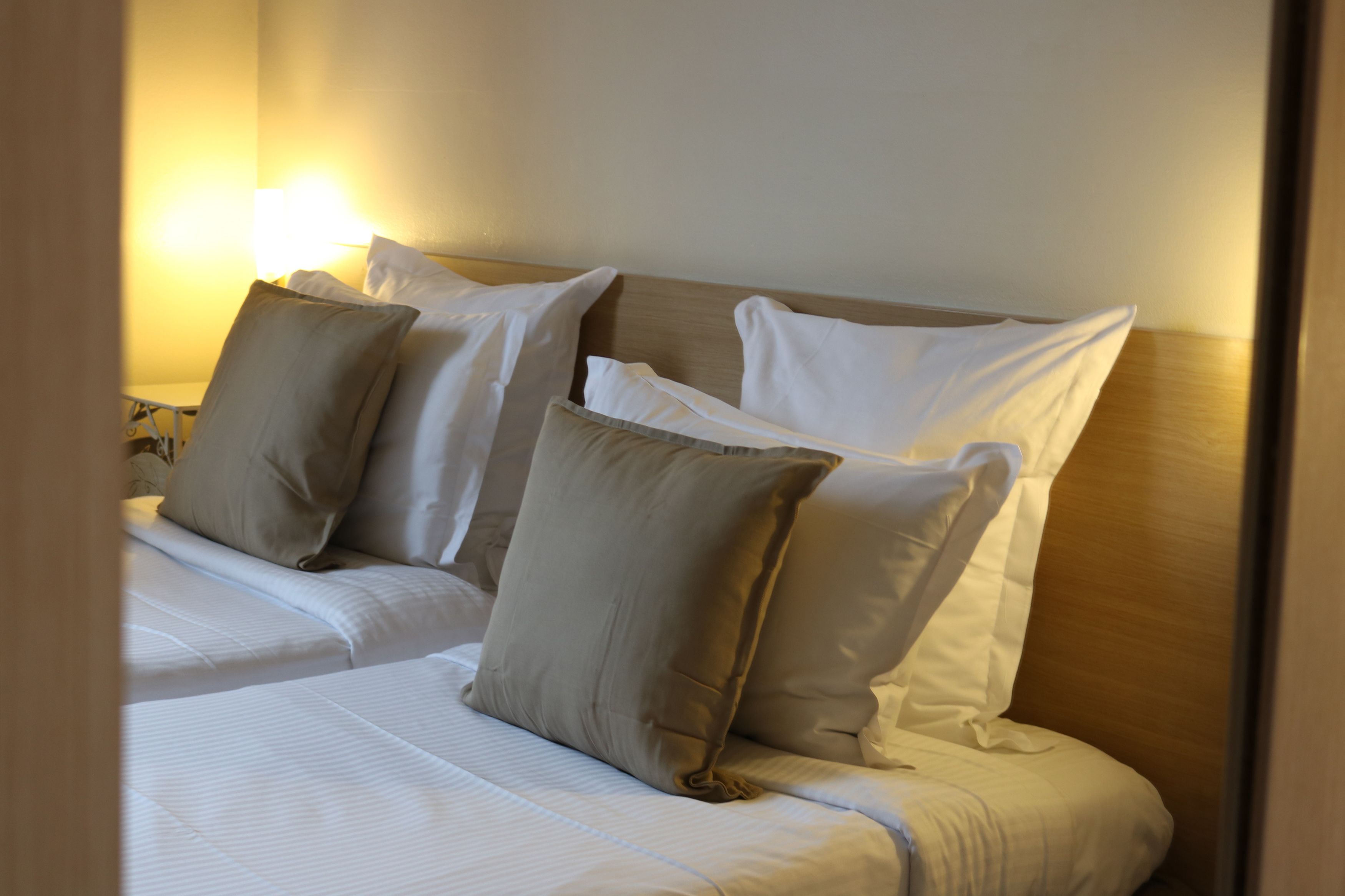 A hotel room with a bed, pillows, and a nightstand with a lamp.