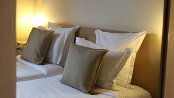 A hotel room with a bed, pillows, and a nightstand with a lamp.