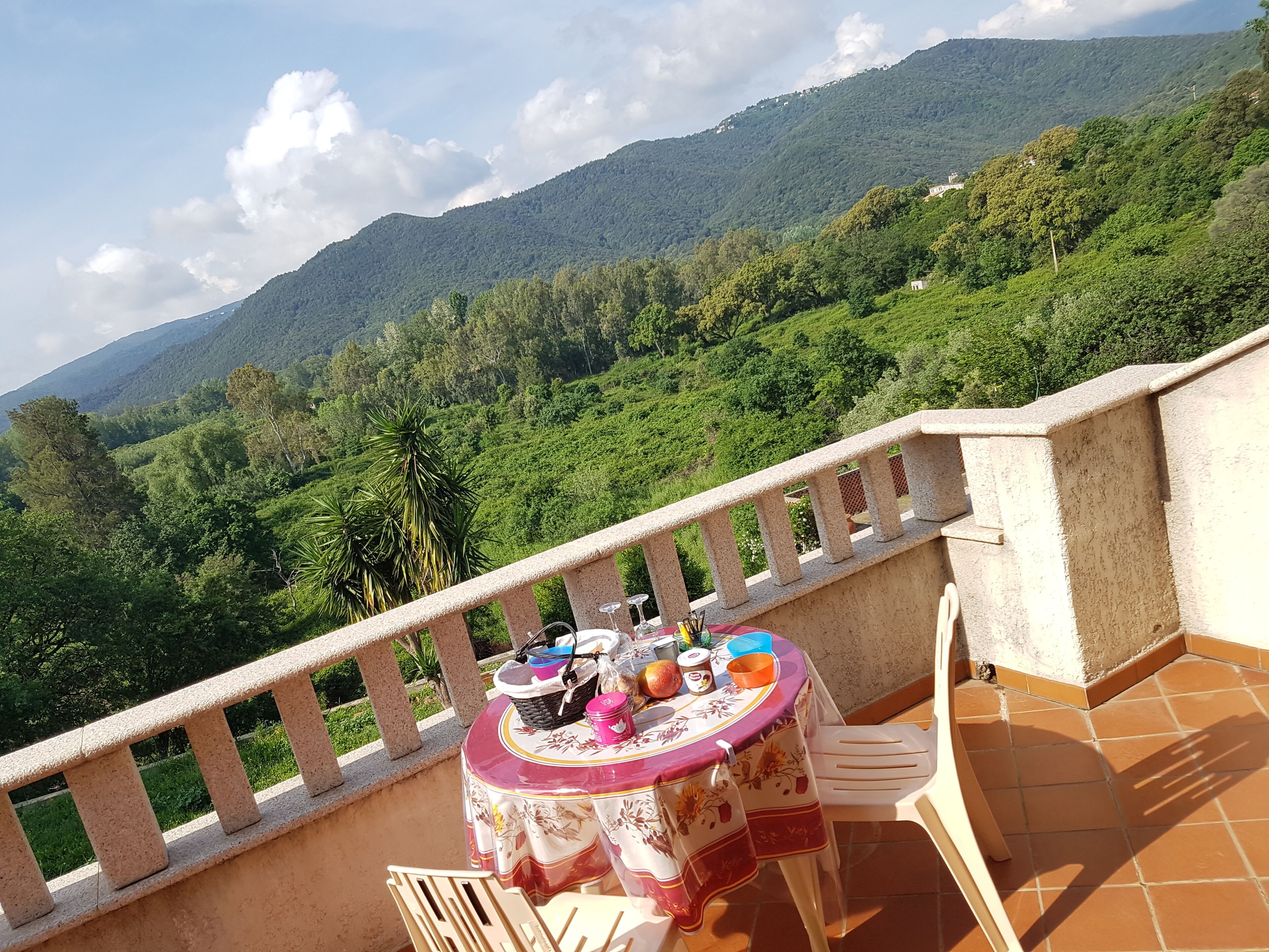 A balcony with a table set for dining, overlooking a mountainous landscape.