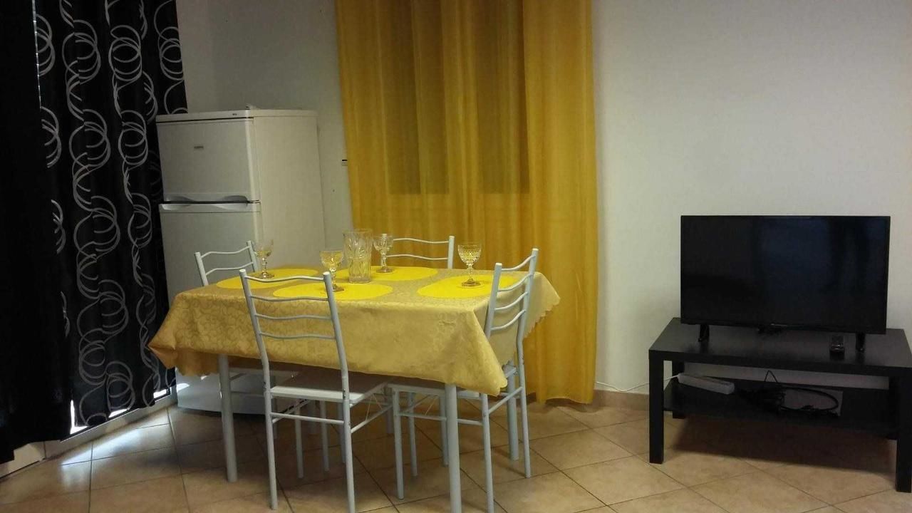 A dining area with a table set for four, a refrigerator, a television on a stand, and a yellow curtain.