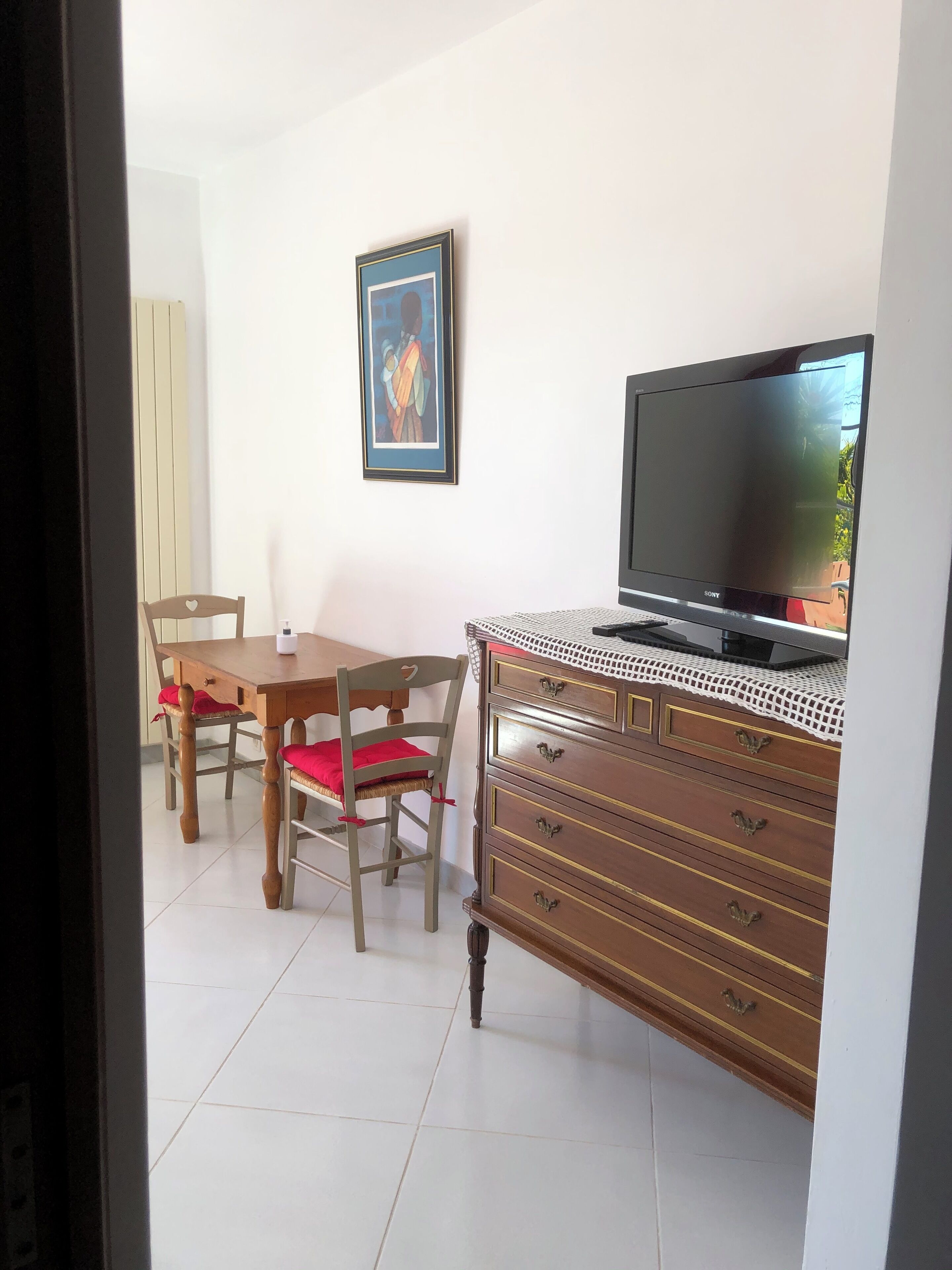 Un comedor con una mesa y sillas de madera, un televisor en un aparador y un cuadro enmarcado en la pared.