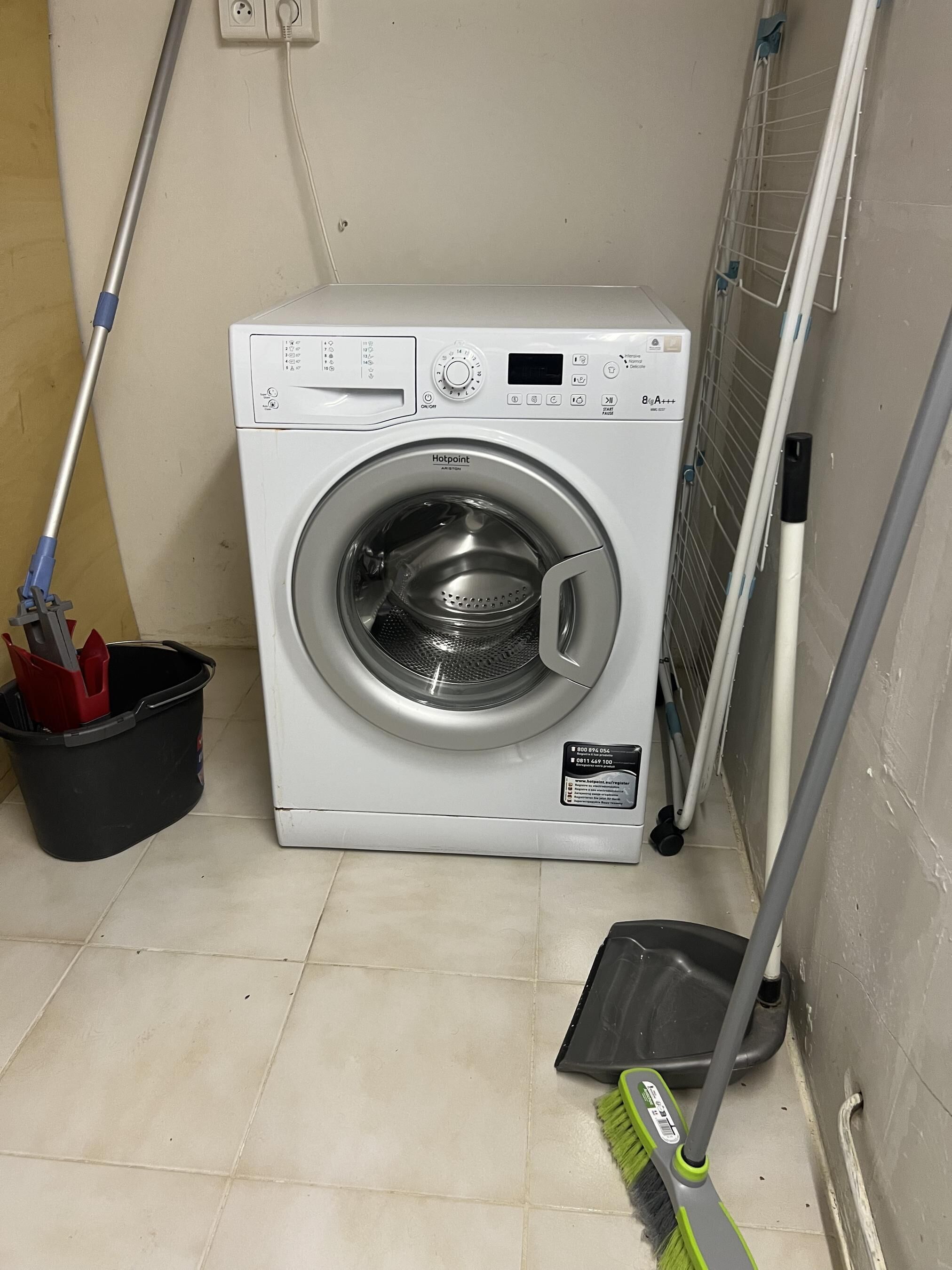 Un lave-linge à chargement frontal doté d’un panneau de commande, une serpillière, un seau et un balai.