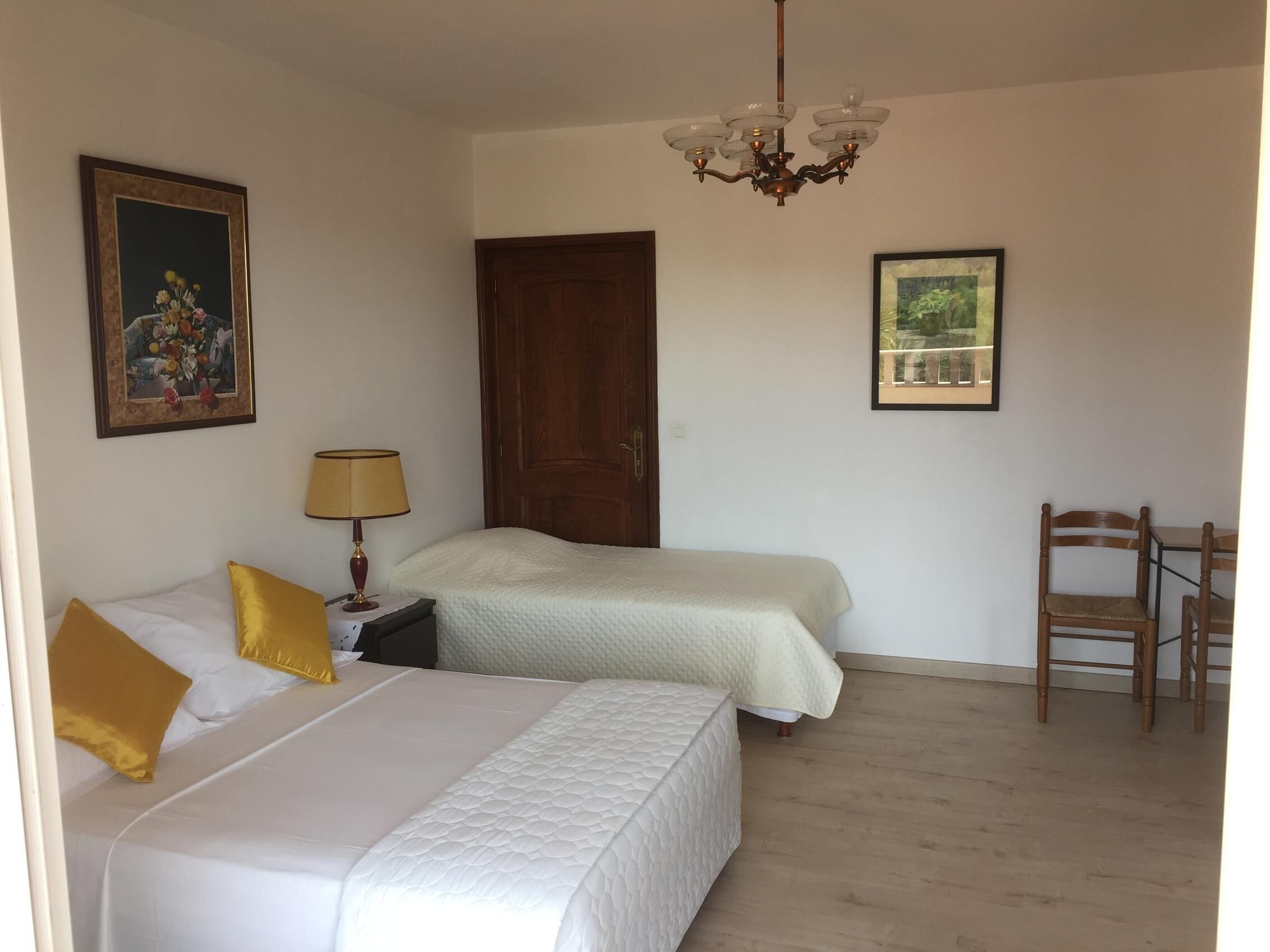 A bedroom with two beds, a wooden door, a chandelier, and a chair.